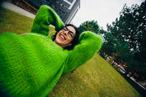 Relaxing in the park, the woman listens to music with headphones on the grass