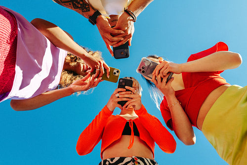 Group of young friends absorbed in smartphones under clear blue sky