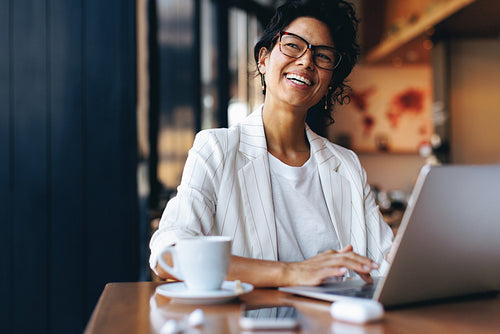 Happy businesswoman working remotely on laptop in a cozy cafe