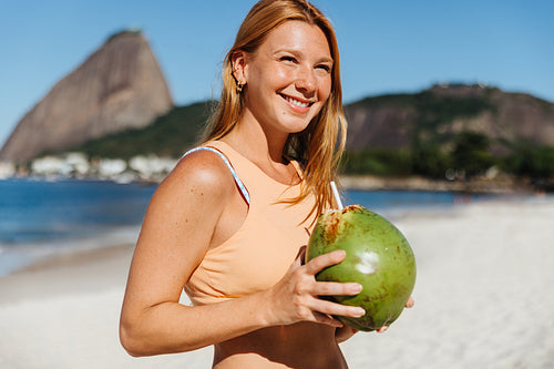 Woman in her 20s enjoying a fresh coconut on the beach with Sugarloaf Mountain in the background