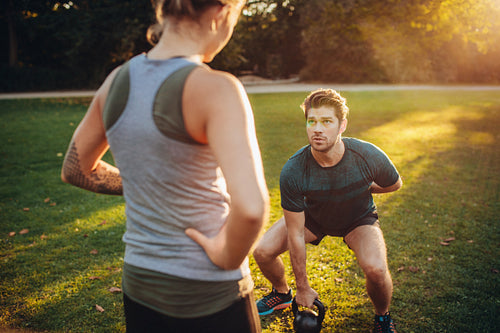 Personal trainer with man doing weight training in park