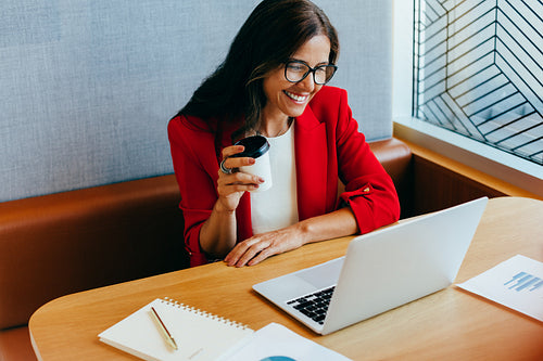 Confident woman in red blazer working on a laptop while smiling
