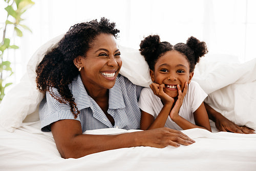 Cheerful mother and daughter playing together in bed