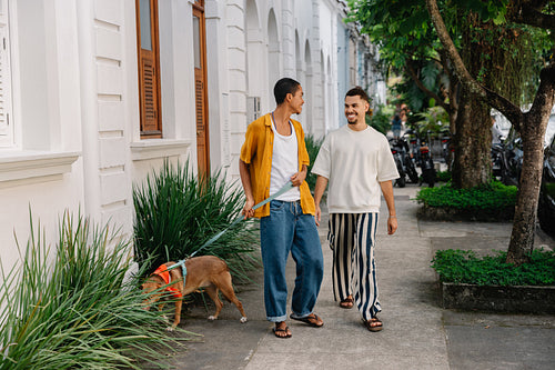 Two men walking a dog together on a city street