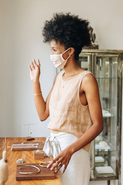 Masked woman in jewelry studio waving at customer outside