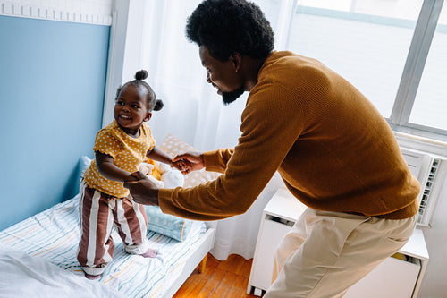Father dancing with toddler on bed at home