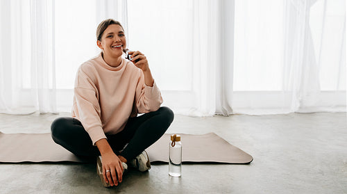Woman enjoying post-workout snack break on a yoga mat indoors