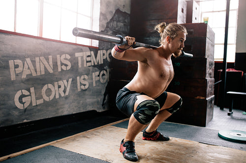 Muscular man doing squats with barbell in gym
