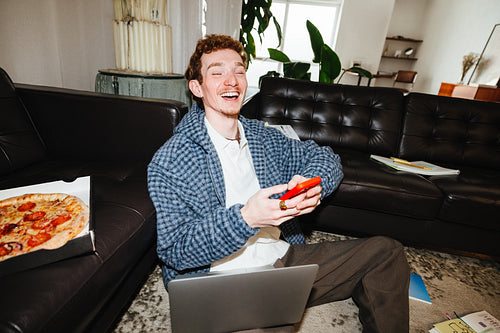 A freelance man works through a casual home session with a laptop and smartphone in the living room.