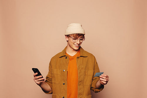 Modern lifestyle: Happy man paying with mobile banking app on peach background