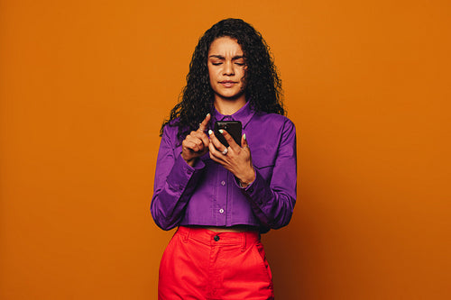 Vibrant woman confused while messaging on orange background with modern smartphone