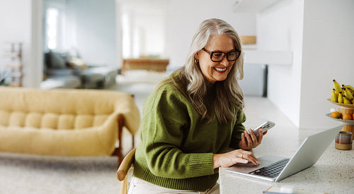 Senior woman uses laptop and smartphone at home