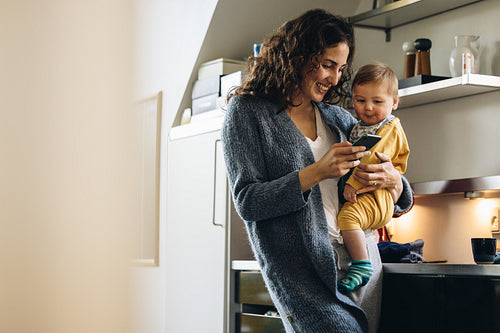 Smiling woman with baby texting on phone at home