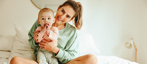 Cheerful mother holding her baby on the bed