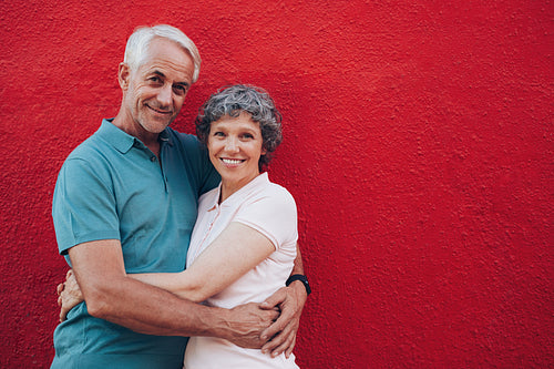 Senior couple embracing against red wall