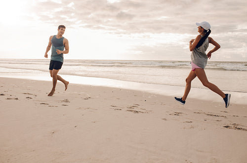 Young man and woman running in morning on beach