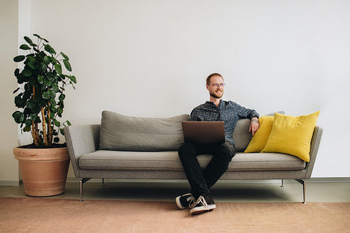 Businessman with laptop sitting on sofa in office