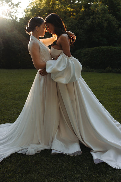 Two brides embracing lovingly in a garden during sunset