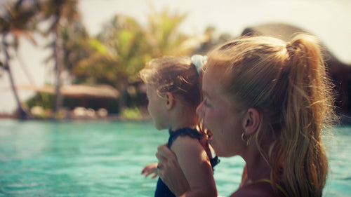 Mother and daughter smiling and laughing together in a beautiful swimming pool on a sunny day