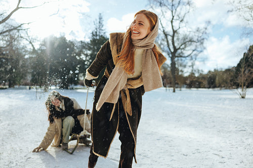 Red-haired woman pulls a sled as friend laughs