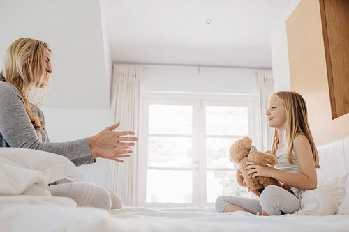 Little girl and woman playing with teddy bear.