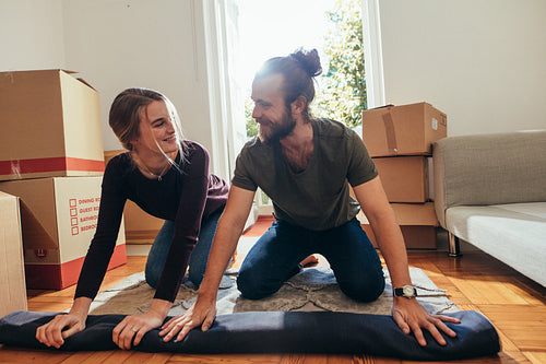 Happy couple rolling a carpet together at home