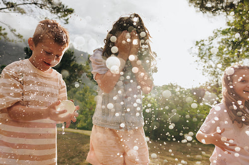 Children playing with water balloons outdoors on a sunny, cheerful summer day