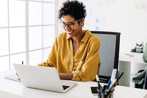 Graphic designer smiles as she works on a laptop in an office