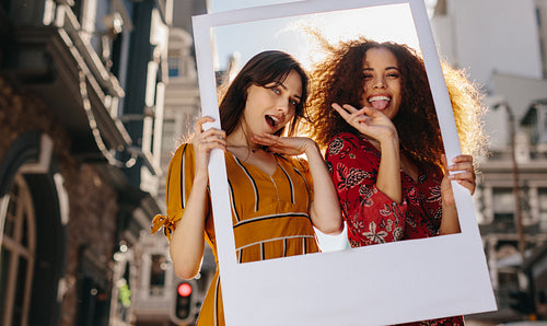 Female friends posing with a blank picture frame