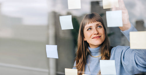 Young female entrepreneur sticking adhesive notes to a glass wall