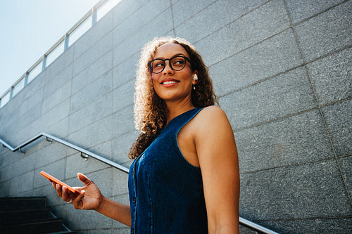 Woman holding smartphone on city stairs during urban commute