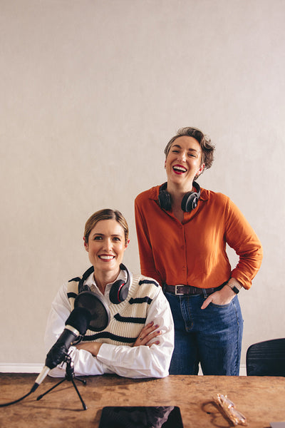 Two female podcasters smiling at the camera in a studio