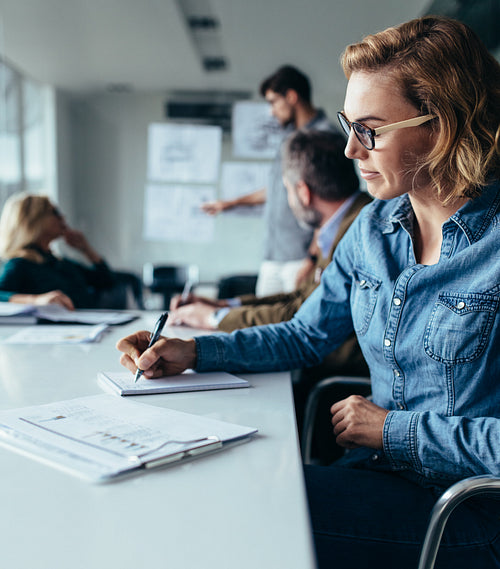 Young businesswoman writing notes during presentation
