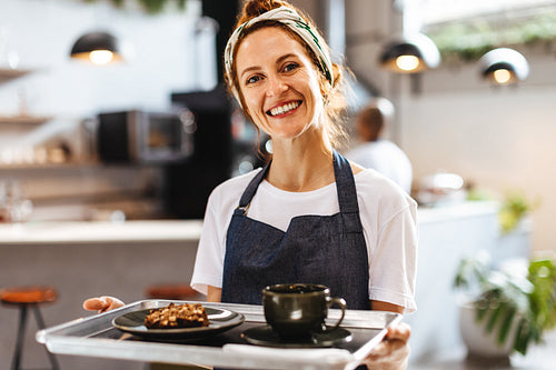 Happy female barista serving coffee in a cafe