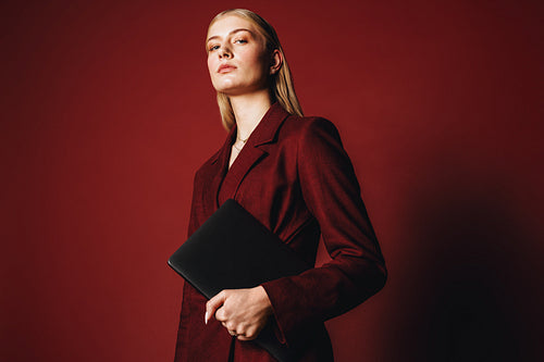 Young entrepreneur in red suit holding laptop with confidence