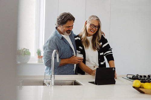 Senior man and woman explore a tablet in the kitchen
