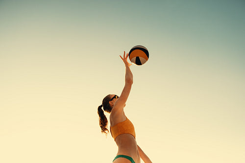 Professional female athlete spiking the ball during beach volleyball championship at sunset