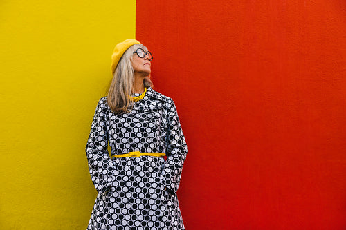 Elderly woman looking away thoughtfully against a colourful wall