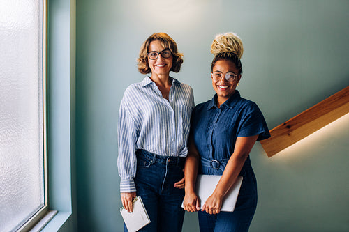 Two women standing together smiling in a casual office environment