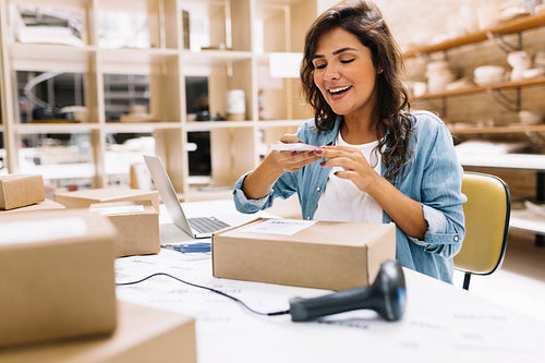 Happy young businesswoman taking a picture of a package box in a warehouse
