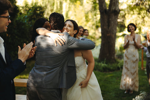 Bride hugging guest during outdoor wedding reception with family and friends