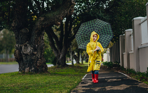 Little girl in raincoat walking with umbrella