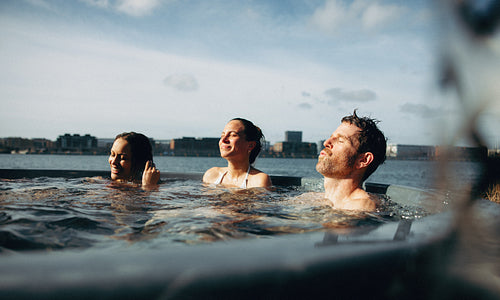 Adults relax in an outdoor hot tub spa by the waterfront for wellness leisure