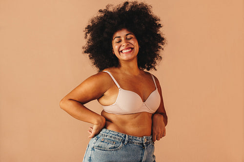 Curvy woman smiling happily while wearing a bra and jeans