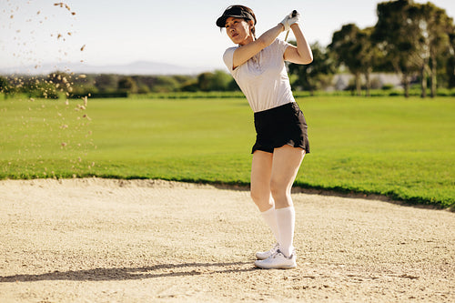 Active woman showcasing her golf swing in a sand bunker on a warm, sunny day