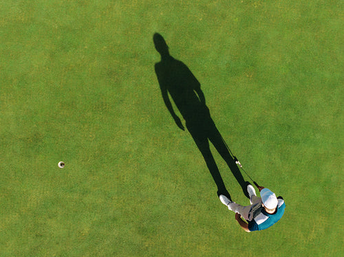 Aerial view of a golfer casting a shadow next to a hole on the green