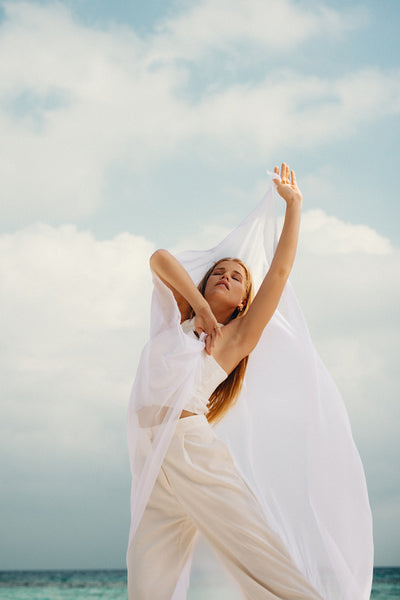Young woman in flowing white outfit enjoying at a serene beach setting