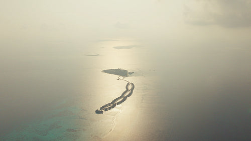 Aerial drone view of luxury overwater bungalows curving into the serene ocean at sunset