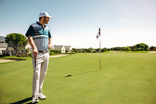 Sportsman leaning on golf club on putting green showcasing a serene golfing landscape