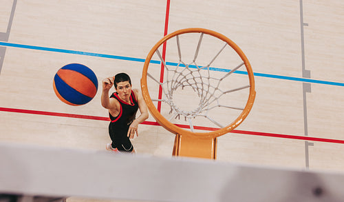 Young female basketball player shooting ball towards hoop in sports gymnasium